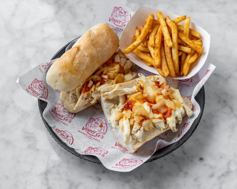 Chicken cheesesteak with onions and sauce, served with fries on Vinny G's branded paper.
