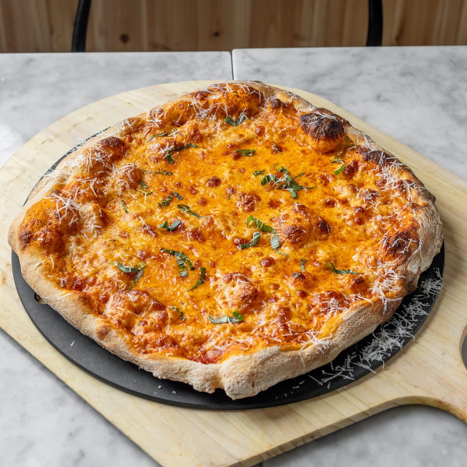 A freshly baked cheese pizza with basil and grated parmesan on a wooden peel.