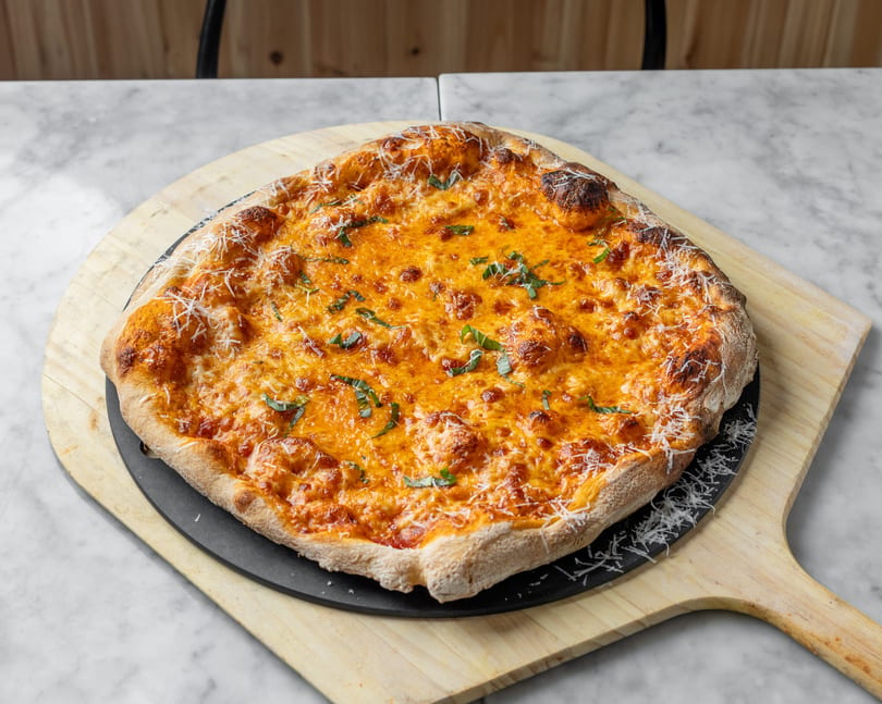 A freshly baked cheese pizza with basil and grated parmesan on a wooden peel.