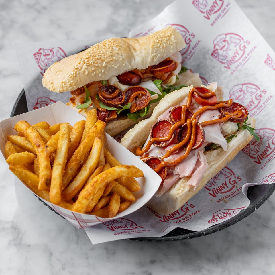 Two Vinny G's subs with pepperoni, ham, and cheese, served with a side of golden fries.