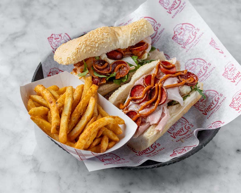 Two Vinny G's subs with pepperoni, ham, and cheese, served with a side of golden fries.