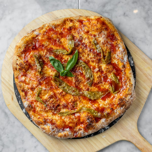 A whole pizza with red sauce, cheese, green peppers, and basil on a wooden peel.