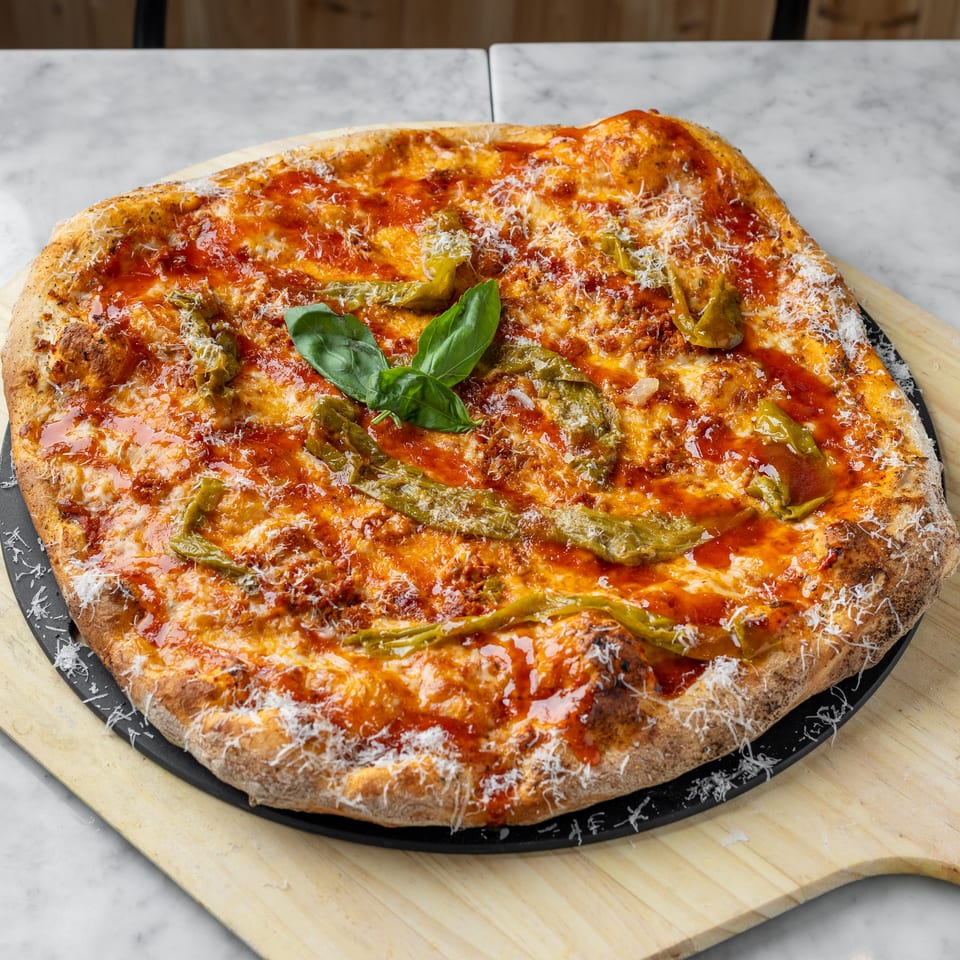 A freshly baked pizza with red sauce, melted cheese, green peppers, and basil on a wooden peel.