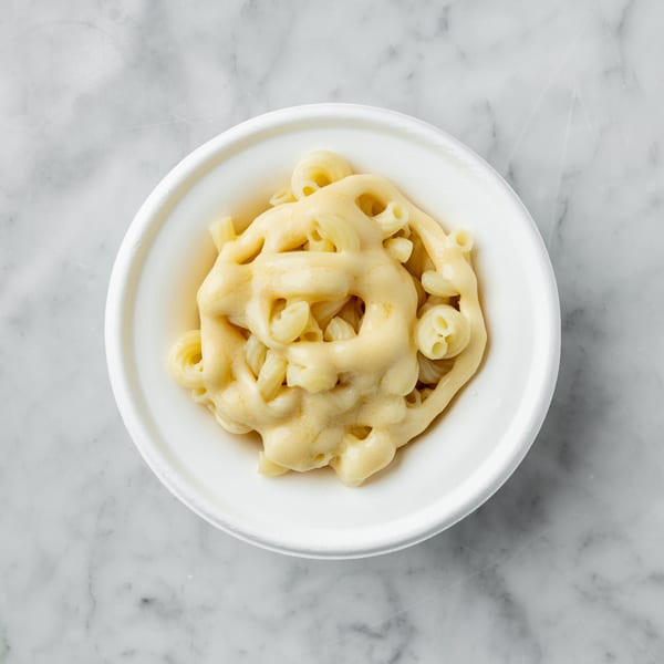 Top-down view of macaroni and cheese in a white bowl on a marble surface.