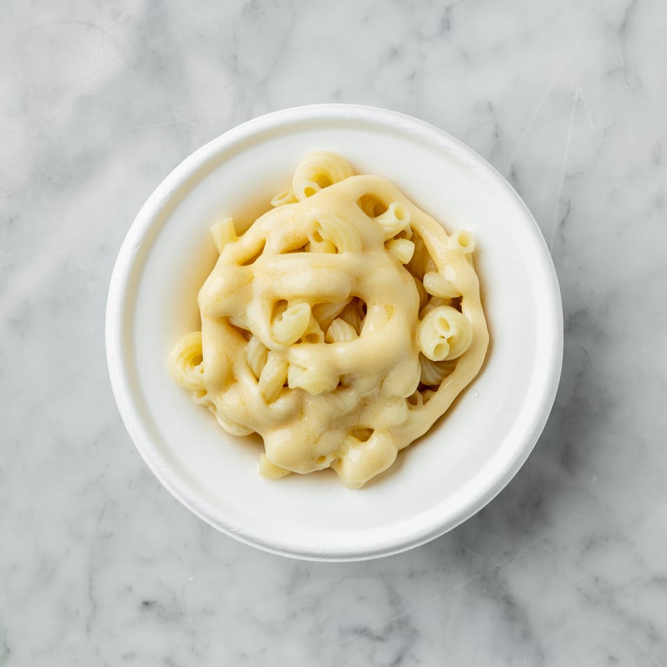 Top-down view of macaroni and cheese in a white bowl on a marble surface.