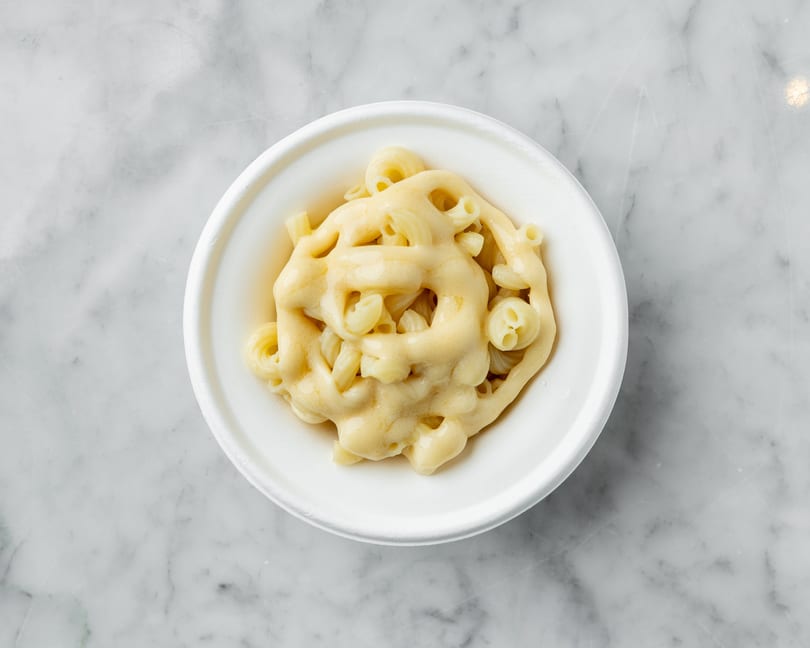 Top-down view of macaroni and cheese in a white bowl on a marble surface.