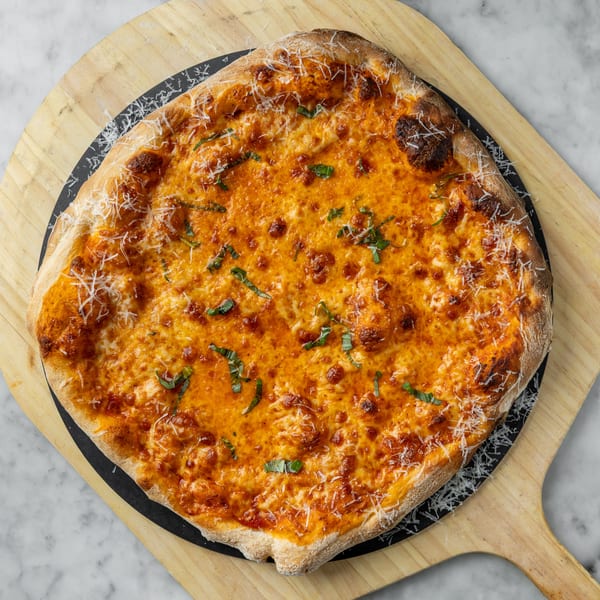A square cheese pizza with basil and parmesan, on a wooden pizza peel.