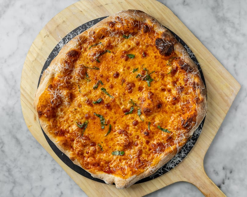 A square cheese pizza with basil and parmesan, on a wooden pizza peel.