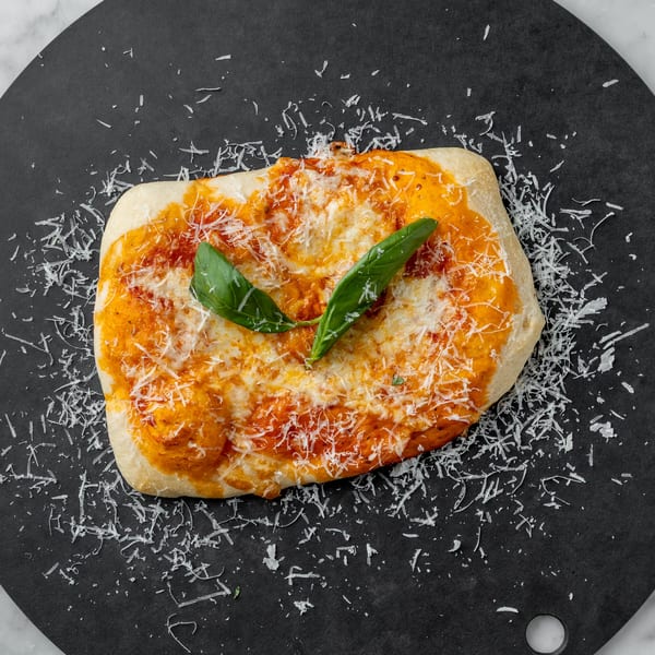 Rectangular flatbread pizza with tomato sauce, melted cheese, grated parmesan, and basil leaves on a black plate.