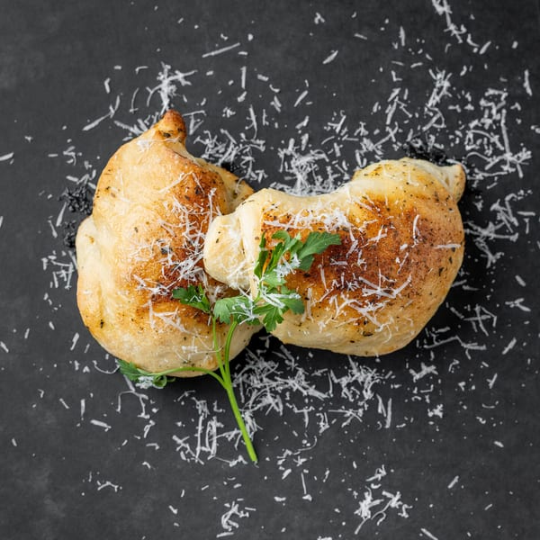 Two golden-brown calzones, sprinkled with Parmesan cheese and fresh parsley, on a dark gray surface.